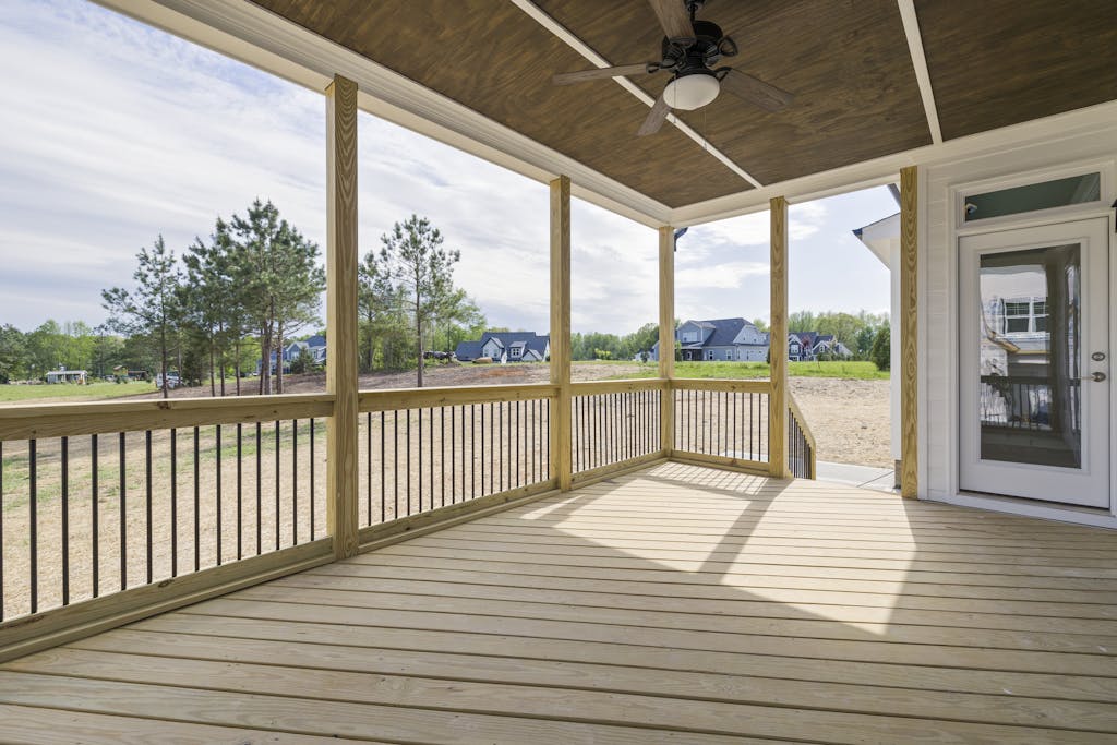 A bright wooden porch with ceiling fan and glass door, overlooking a grassy area.
