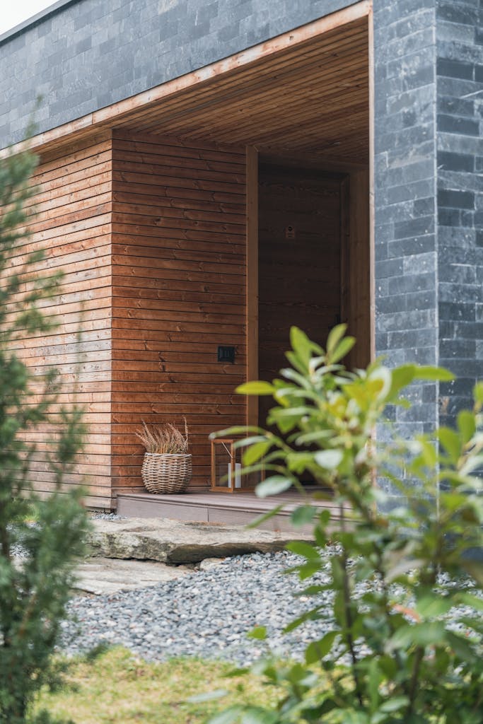 A serene entrance of a modern wooden house surrounded by greenery.