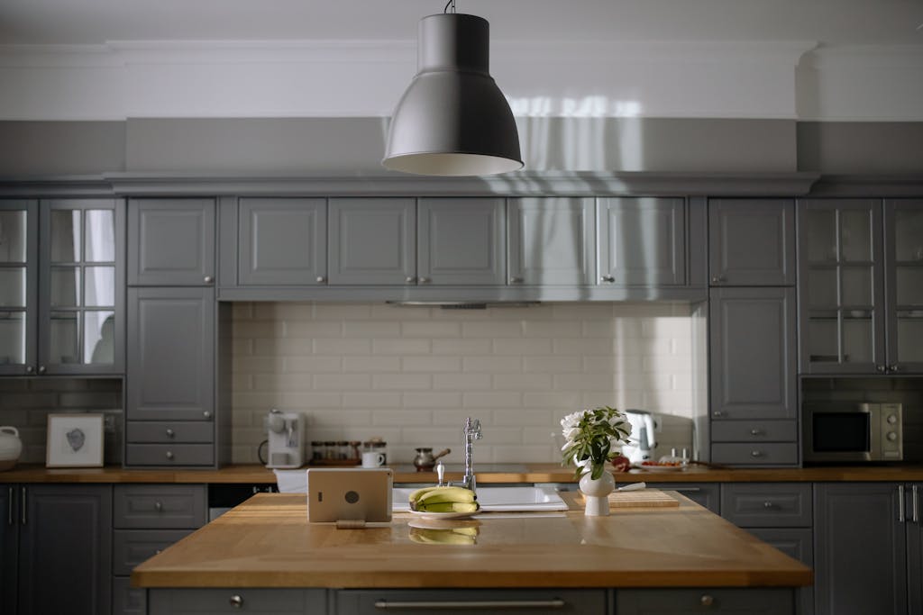 A sleek kitchen with gray cabinets, wooden countertops, and modern lighting.