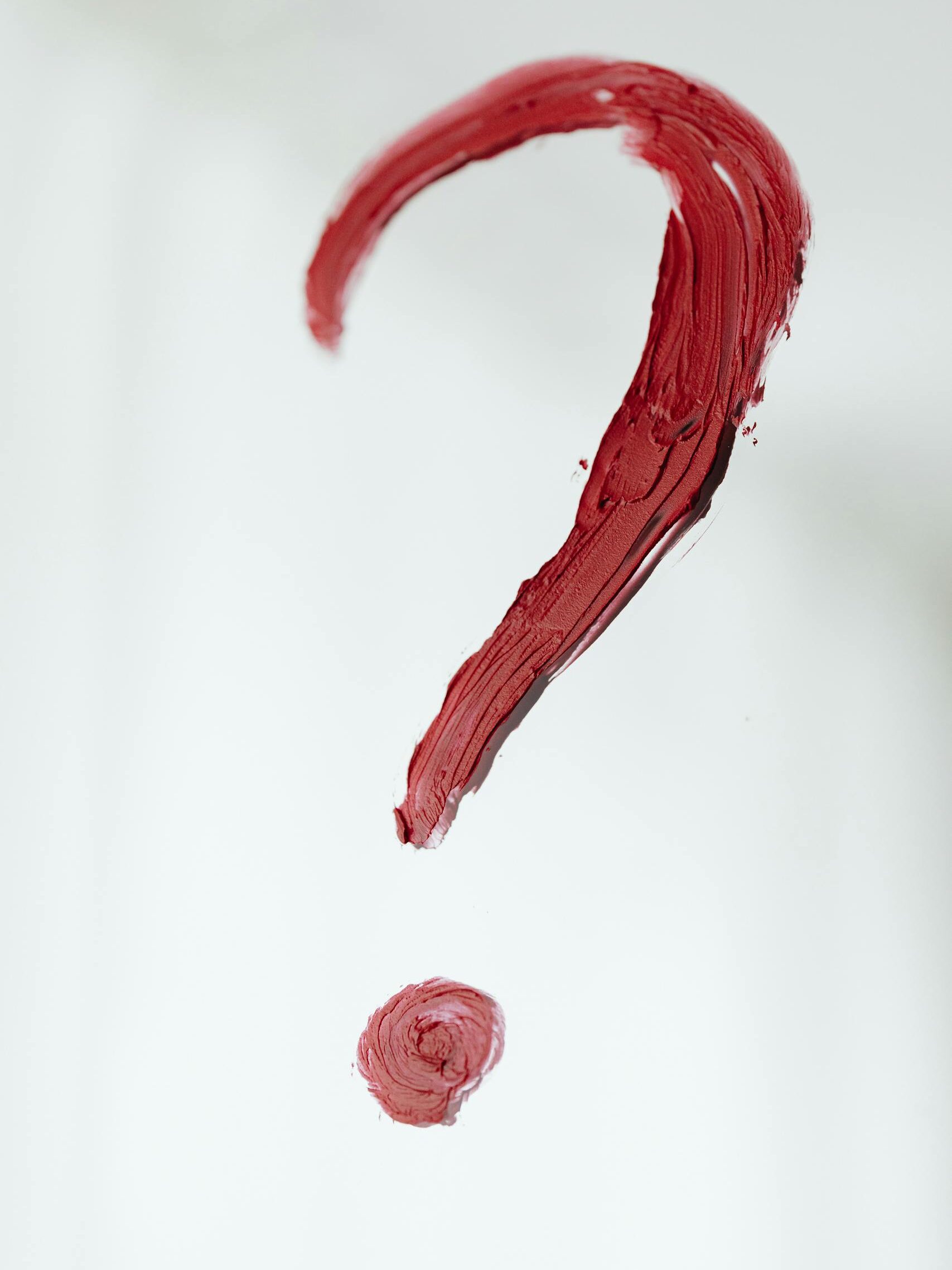 Close-up of a red painted question mark on a white background. Conceptual and abstract art.